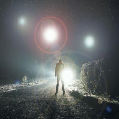 A silhouetted figure looks up at glowing orbs floating above a misty road.