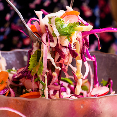Closeup of someone using fork to pick up slaw from copper serving dish.