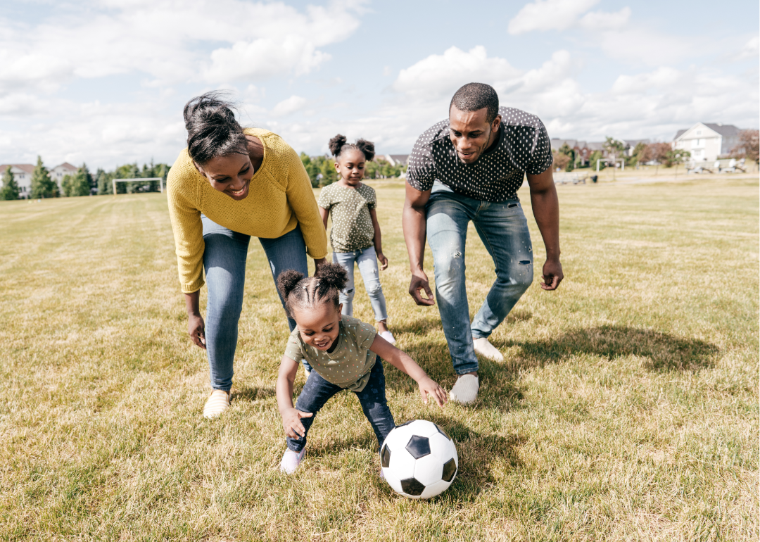 Family with two children playing soccer in a suburban neighborhood