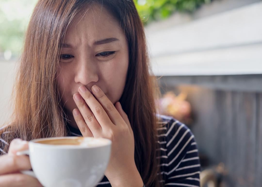 Woman holding a hot coffee, covering her mouth because it tastes bad.