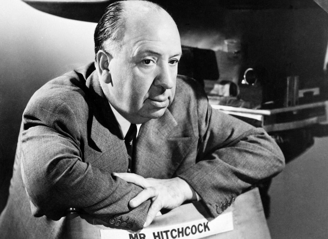 Alfred Hitchcock leaning over a director's chair with his name on it.