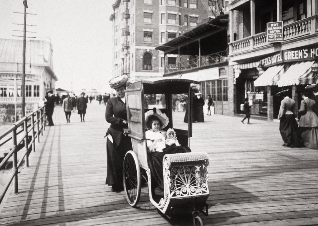 Woman pushing an elaborate wicker carriage holding a young girl and her doll in Atlantic City on the boardwalk in New Jersey in the 1890s.