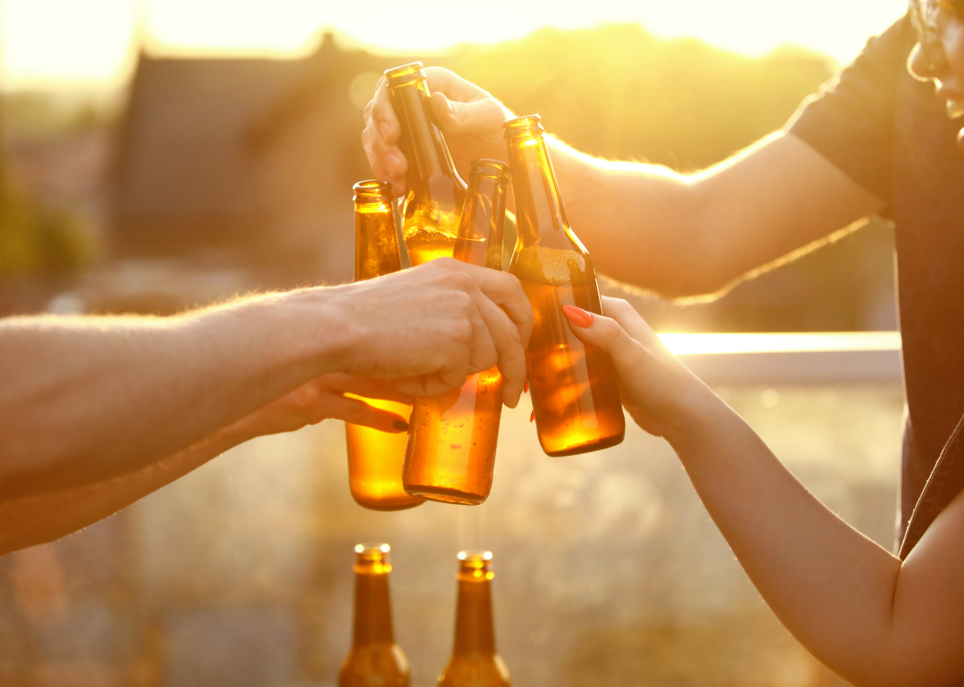 People toasting with beer bottles as the sun glows behind them.
