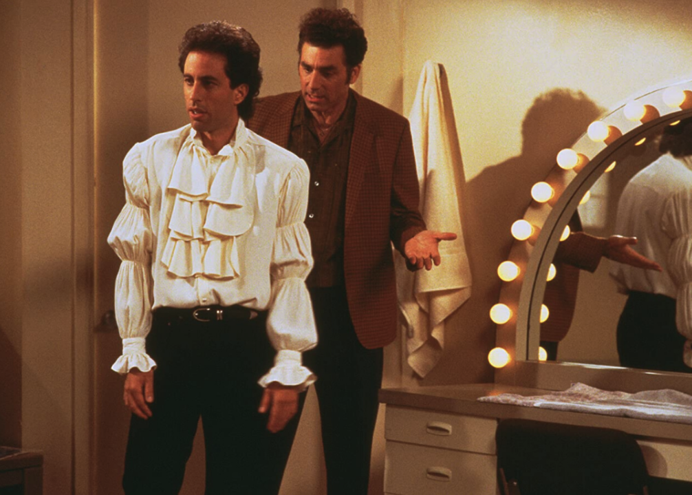 Jerry wearing a ruffled shirt with Kramer behind him. 