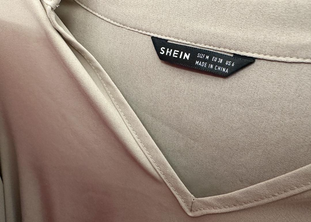 A Shein clothing brand tag in a tan v-neck shirt.