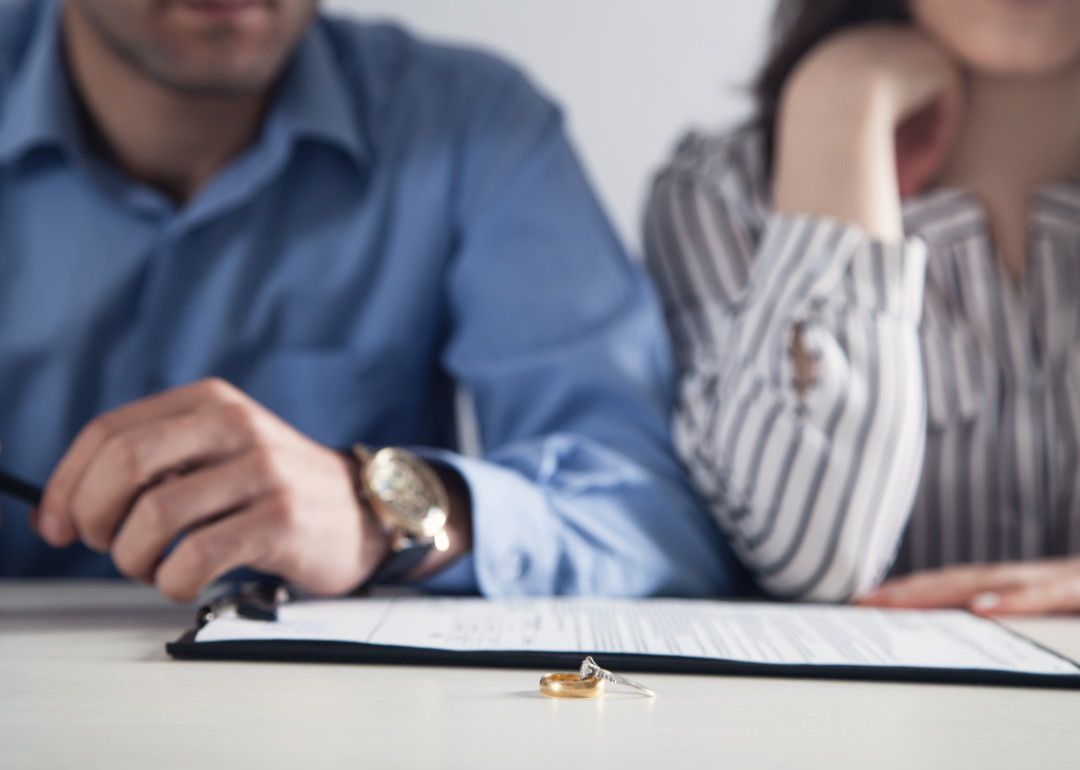 Couple sitting in front of a table with divorce papers and wedding rings atop it.