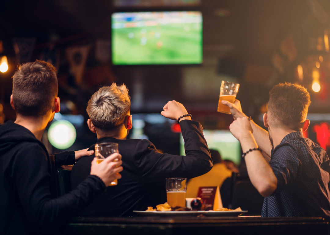 Three friends cheering as they watch TV in a sports bar.