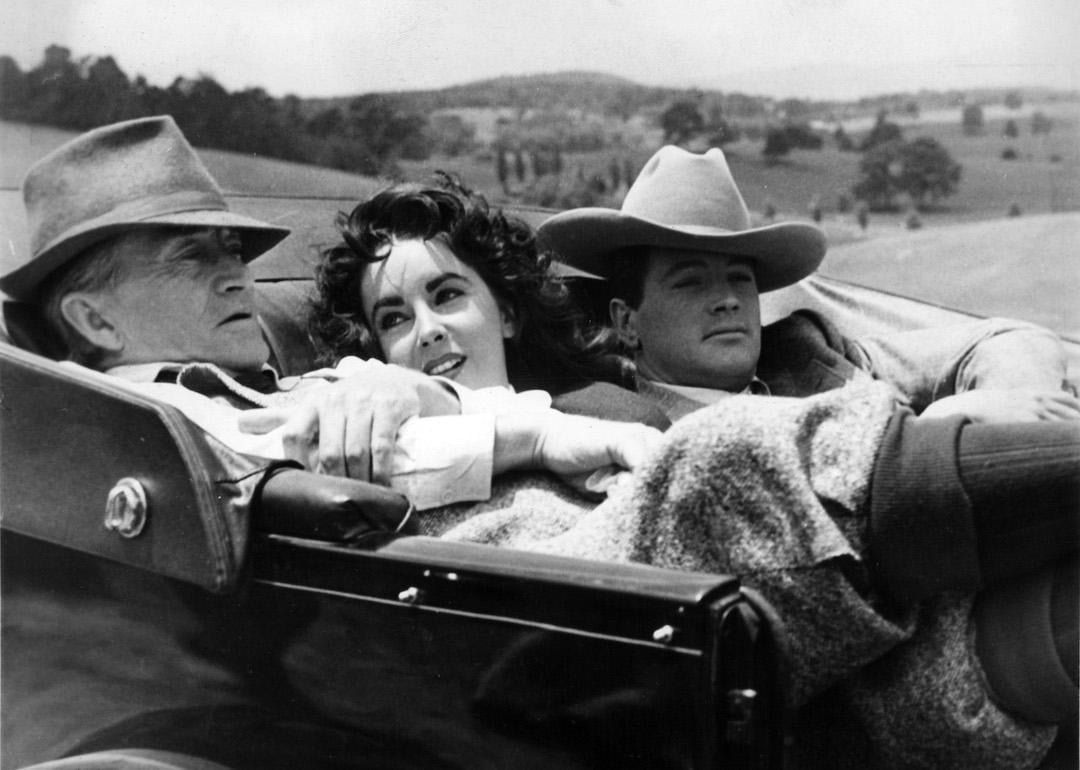 Actors Paul Fix, Elizabeth Taylor, and Rock Hudson reclining in a car on the set of the 1956 Western film 'Giant.'