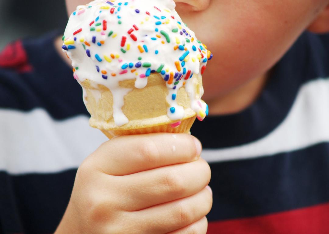 Closeup of kid holding a cone of vanilla ice cream with rainbow sprinkles or jimmies.
