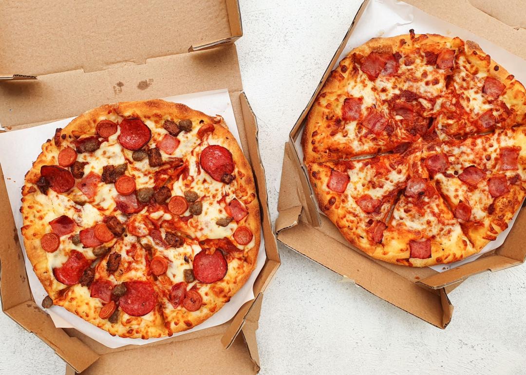 Two different types of pan pizzas in delivery boxes sitting on a table.
