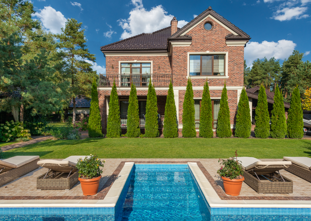 A large brick home with immaculate topiaries and a pool in the foreground.