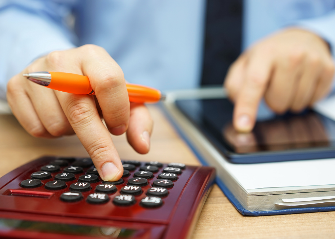 A person operates a tablet and calculator side by side.