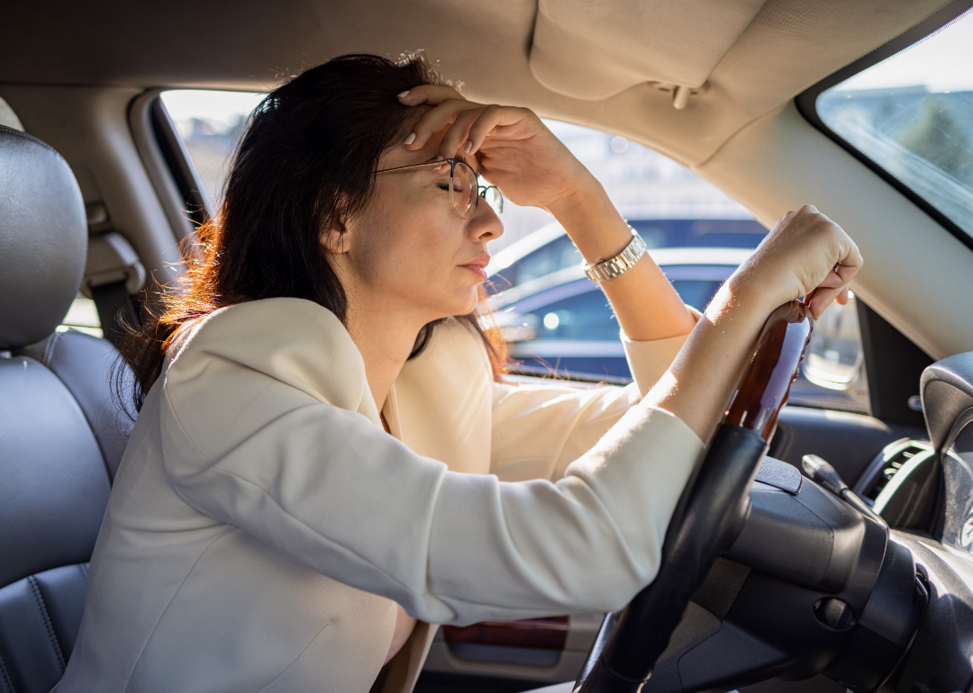 A woman sits at the wheel of her car looking stressed.