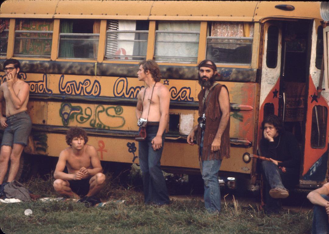 Near the 'Free Stage' at the Woodstock Music and Arts Fair, people lean against a decorated school bus used by the Hog Farmers, a group who had been asked to help construct, ensure security, and provide food for the event, Bethel, New York, in August 1969.