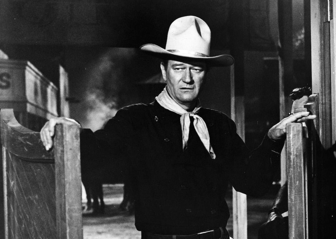  Actor John Wayne wears a pistol in a holster and stands in a doorway in a still from the 1962 Western film 'The Man Who Shot Liberty Valance.'
