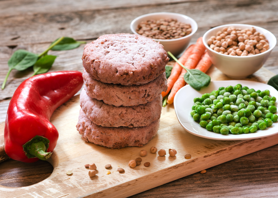 A stack of uncooked, plant-based burgers on a chopping block.