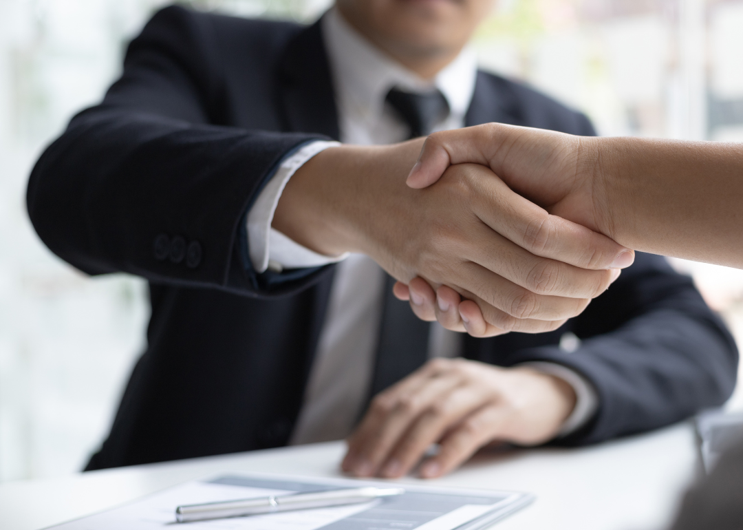 Person in a suit shaking the hand of a prospective employer at a job interview.