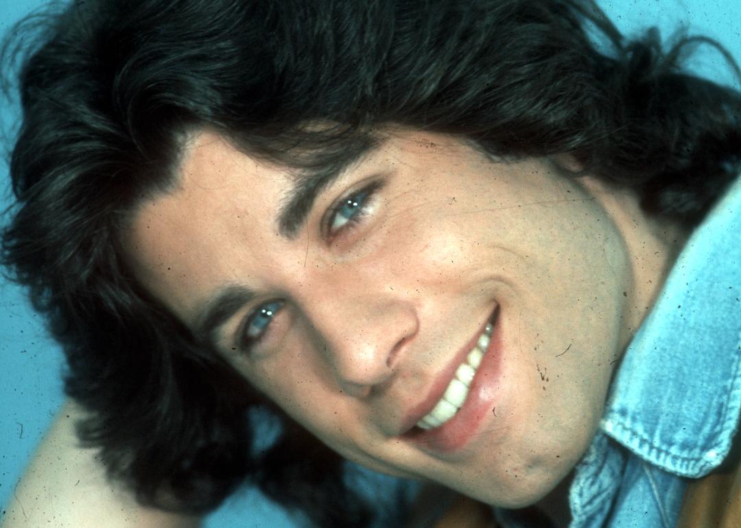 Young John Travolta in a denim shirt and tan vest poses for a portrait circa 1970.