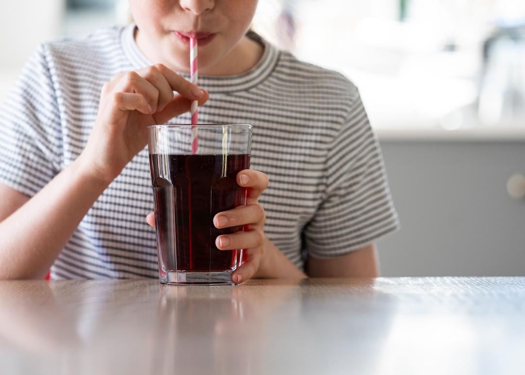 Closeup of kid drinking a soda from a white and red straw.