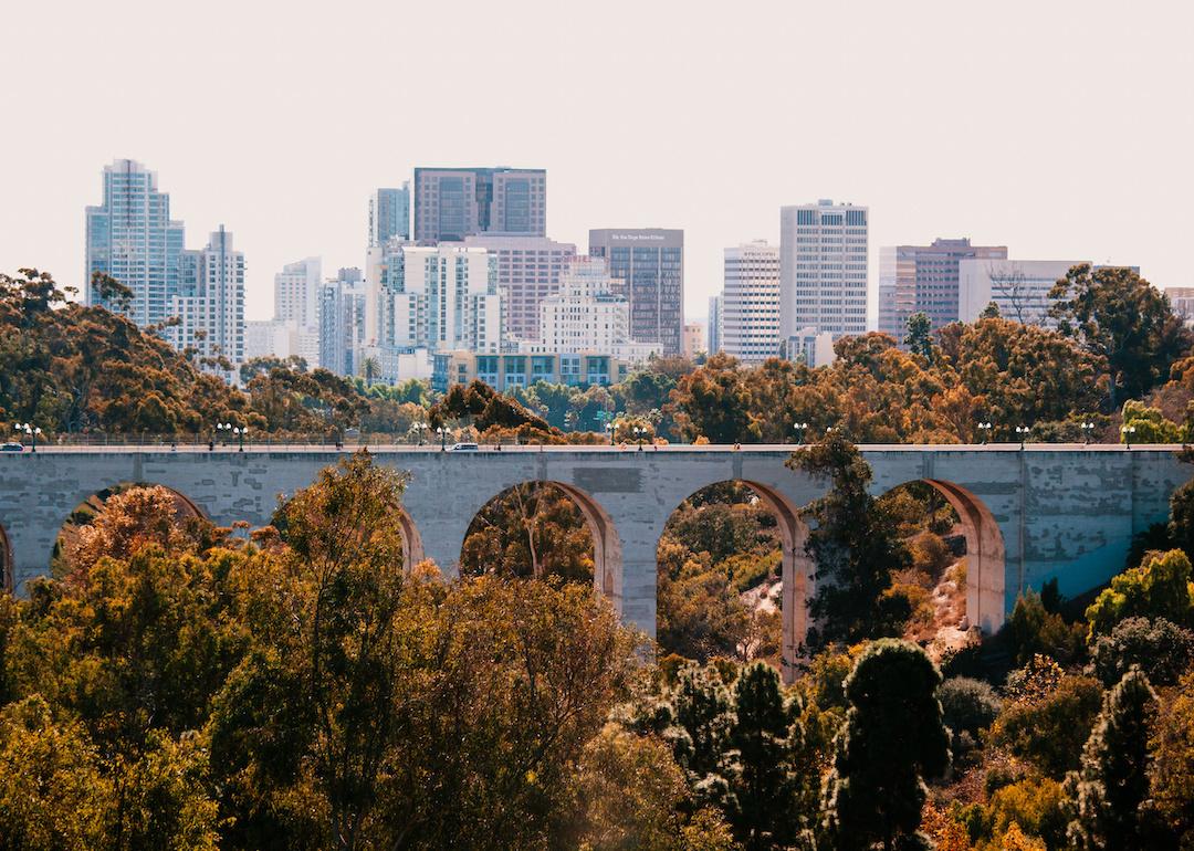 A view of the bridge with Balboa park and foliage in front of the San Diego skyline.
