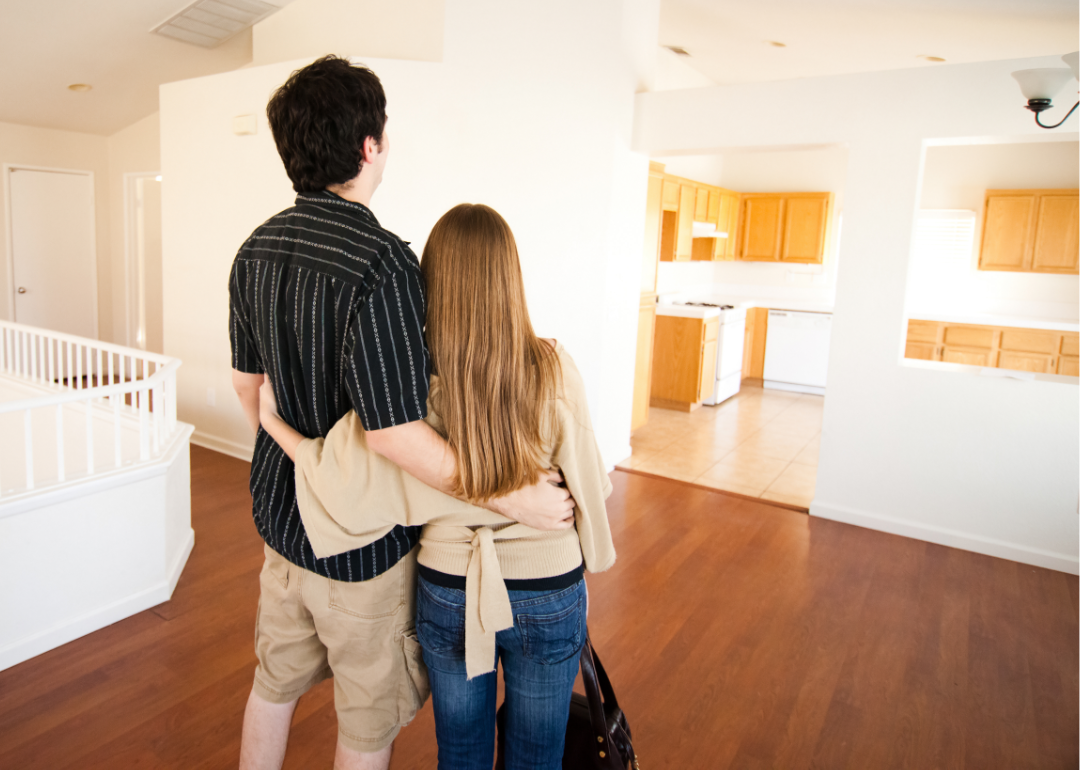 Young couple with arms each other stand looking at empty new home.