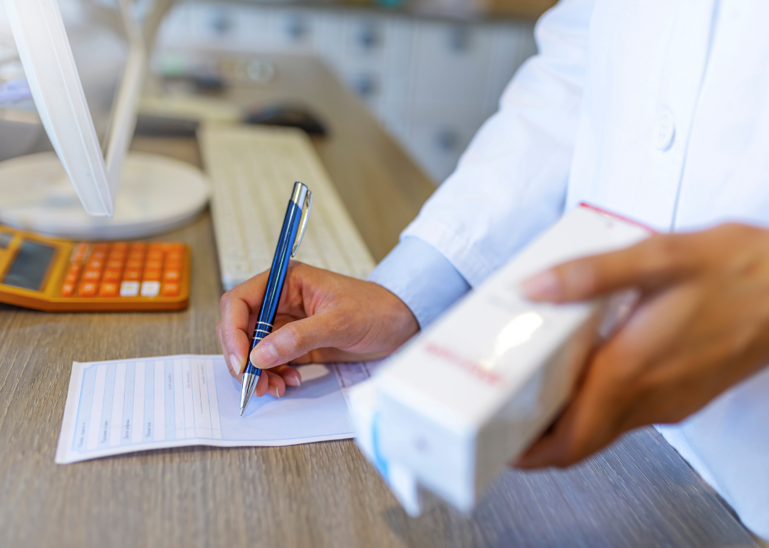 Closeup of a doctor's hands as they write a prescription and hold a box of medication.