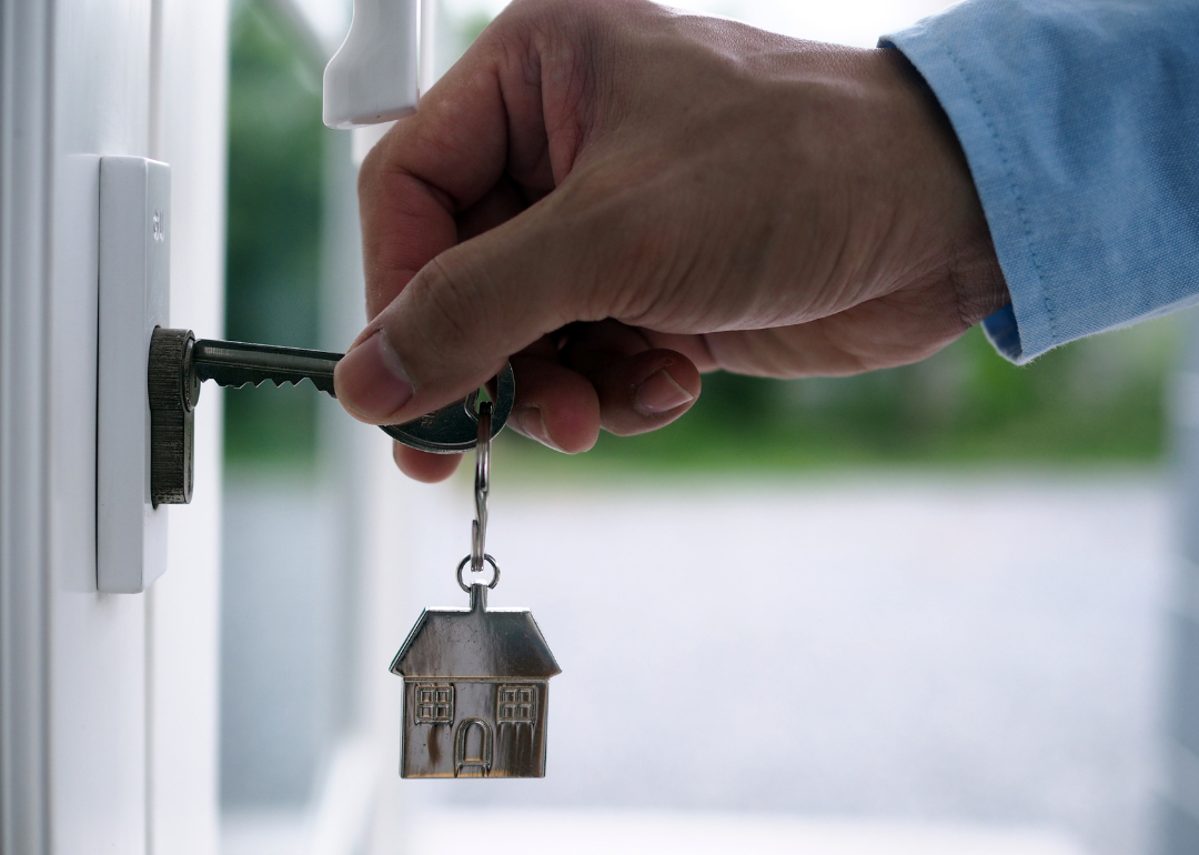 Homeowner inserting a key attached to a keychain with a house-shaped charm on it into a front door lock.