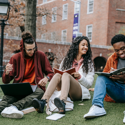 A group of three multiethnic students sit together on a college quad