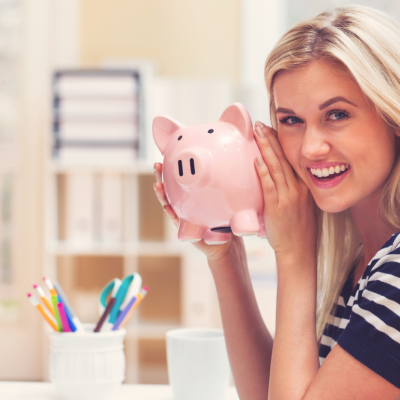 A young blonde woman in a striped shirt smiling an holding a piggy bank