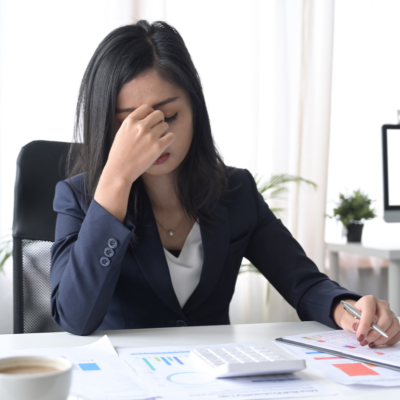 A businesswoman seated at a desk holds a hand to her face in worry.