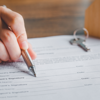A rental agreement form that a landlord is resting a pen against to show details to a presumed tenant