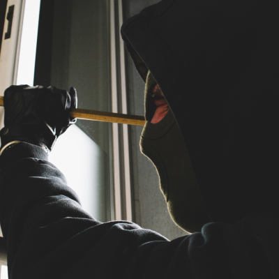 A burglar clad in black uses a crowbar to break into a home through a window casing