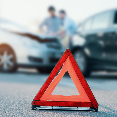 A red triangular hazard sign sits on the road near an auto crash