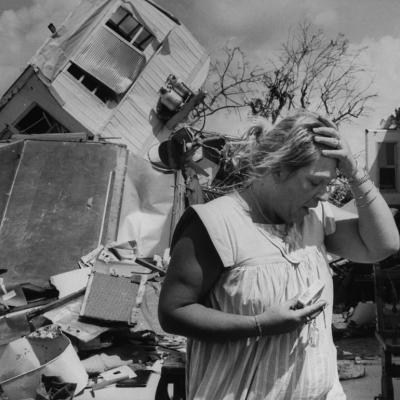 A stunned mobile home owner puts their hand on their forehead in despair in front of the overturned wreckage of their residence after the wrath of Hurricane Andrew in 1992.