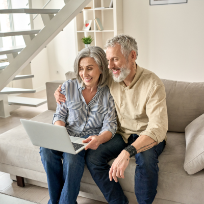 A senior couple sit on a beige couch and look at a laptop computer