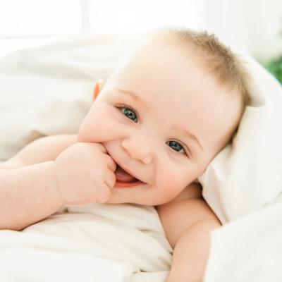Smiling baby with blue eyes wrapped in a white blanket.