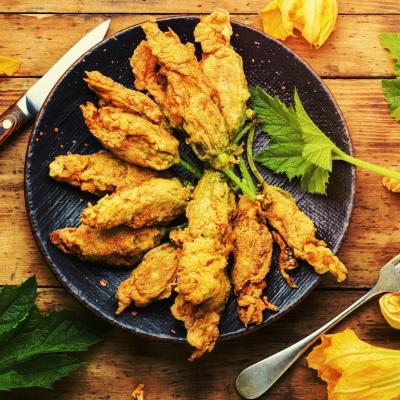 Fried squash blossoms stuffed with cheese on a black plate on a wooden table.