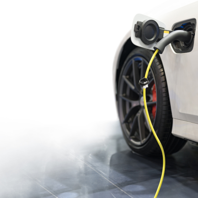 An electric vehicle plugged in to charge with smoke in the background to signify a possible battery fire