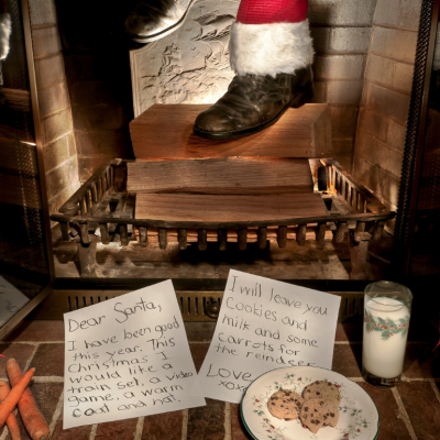 Santa's feet emerging from a chimney with a letter to Santa and cookies in the foreground