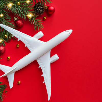 A conceptual image of a white airplane model against a red background with holiday foliage