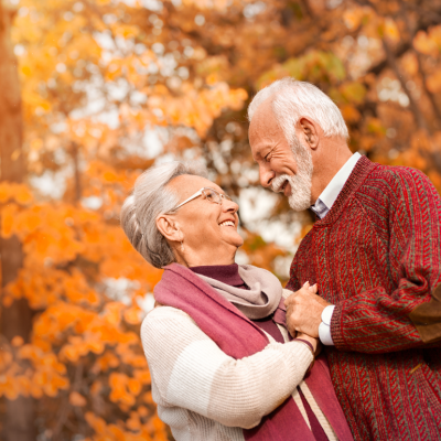 An older couple smile at one another with a fall background