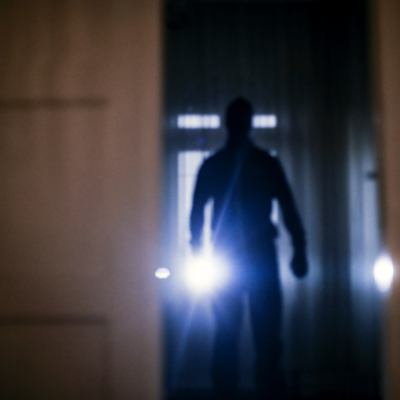 A blurred image of a burglar with a flashlight entering a home 