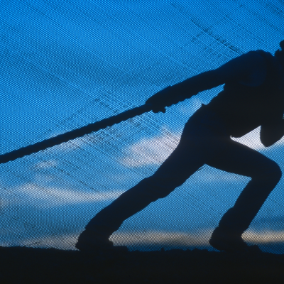 Silhouette of construction worker in a hard hat pulling on a rope.