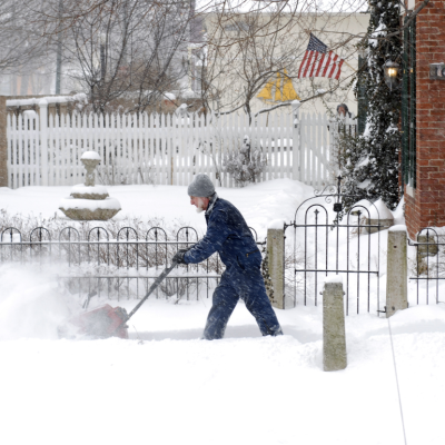 Man with a snow blower walking through a snow-covered sidewalk