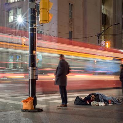 unhoused person sleeps on the streets in Toronto with motion blur of traffic driving by