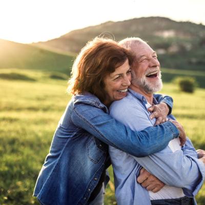 Side view of senior couple hugging outside in nature at sunset.