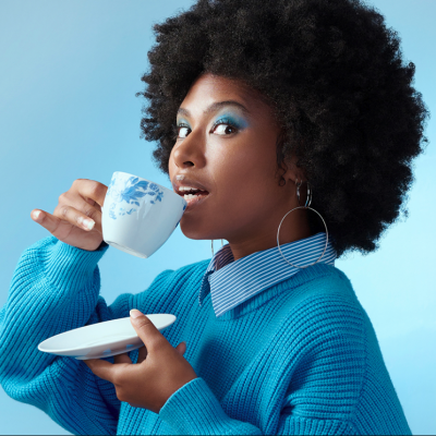 A Black woman with a teacup against a bright blue background.