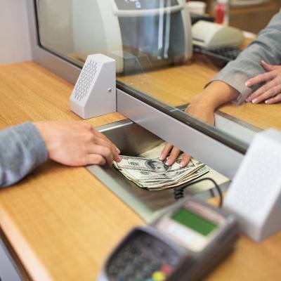 View of cash exchange in window between hands of teller and bank customer