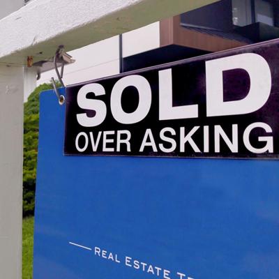 close up of "Sold over asking" sign in front of house
