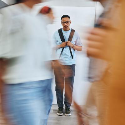 serious young man standing in school hallway with backpack with motion blur of students passing in front 